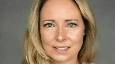 PHA Catherine McKeown pictured with long blonde hair. She is smiling and standing in front of a grey screen (for a company photo)