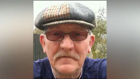 Hertfordshire Constabulary Keith Whiting wearing a hat and glasses. He has a moustache and is wearing a navy blue top