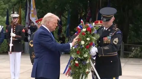 Donald Trump puts his hand on a wreath