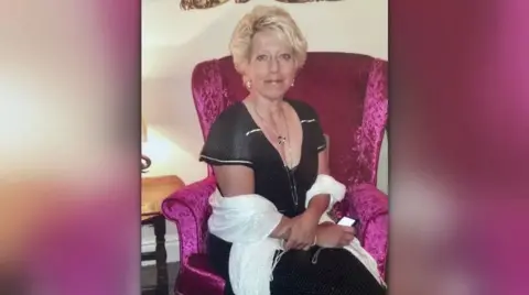 Family handout A woman with short blonde hair sits on a pink armchair. She is wearing a black and white dress, silver earrings and necklace and has a white shawl around her arms.