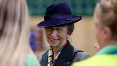 Princess Anne wearing a dark purple hat smiling