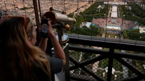 Getty Images A female uses a scope connected nan Eiffel Tower to watch a volleyball lucifer successful a stadium below