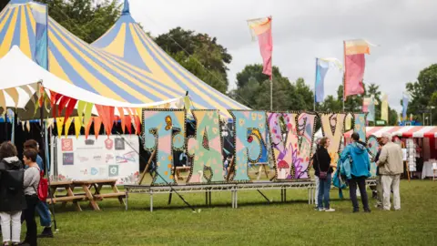 Menter Caerdydd The Tafwyl sign in a field with tents in the background and people gathered chatting in groups