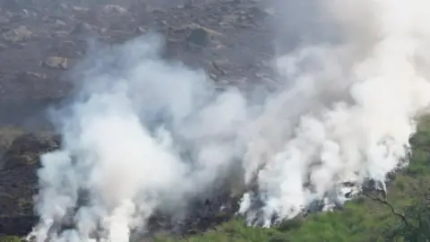 Smoke can be seen billowing off moorlands after a fire quickly spread in the area. Patches of burnt grass be seen on the moorlands. 