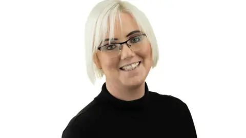 Fletchers Solicitors Francesca Paul has very white/blonde hair, dark eyebrows and is wearing black rimmed glasses. She is wearing a black polo neck jumper in contrast to the photo's pure white background. 