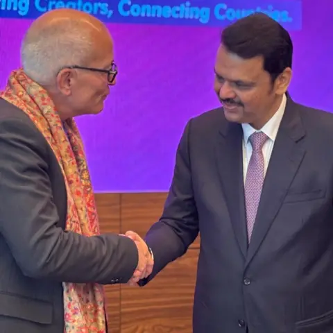 University of York A bald man wearing black spectacles and an orange paisley scarf shakes hands with a man in a suit and purple tie.