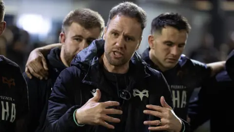 Ospreys head coach Mark Jones gestures with his hands as he talks to his squad in a huddle