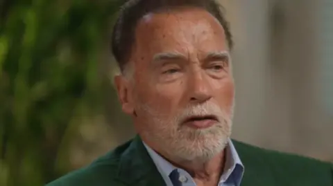 Arnold Schwarzenegger speaking to the BBC, wearing a green suit jacket