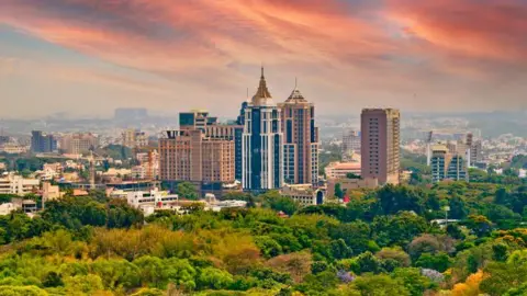 Getty Images Bangalore City Aerial View with skyscrapers behind a rug of green cap, and the sky with amber color.