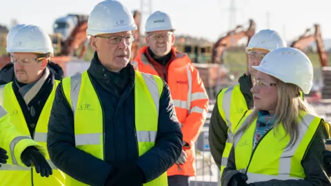 PA Media John Swinney, wearing a yellow hi-vis jacket and white hard hat, poses with several similarly dressed members of the CIP team at the construction site at Colburn 1.