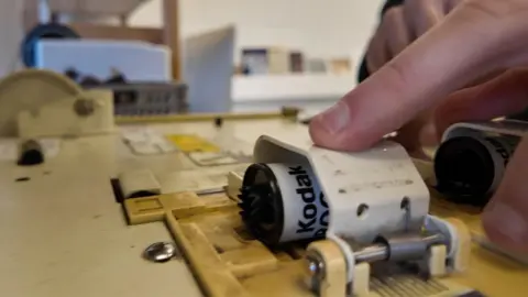 A film roll i s in a machine with a hand on top of it.