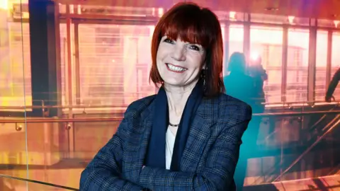 A woman in a plaid blazer with short red hair.