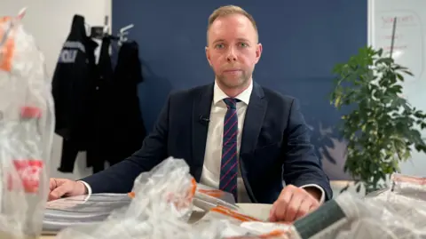 DS Chris Barrow sitting at a table with evidence bags in front of him containing Vlad's suicide kit, as he warned of the risk of people on the website being groomed into harming themselves