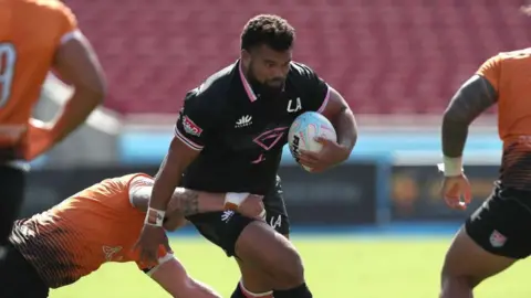Marco Fepulea'i running with the ball under his left arm while a player tackles him around his waist during a game for LA Giltinis in 2022