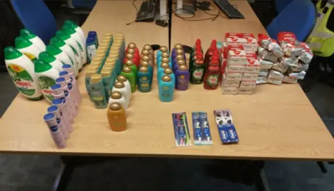 Cambridgeshire Police There are lots of different things lined up on a wooden table, including deodorants, shampoos, washing up liquid and bags of coffees.
