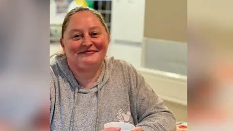 Chantel smiles in a zoomed in shot from inside a white-painted kitchen while holding a white mug. 