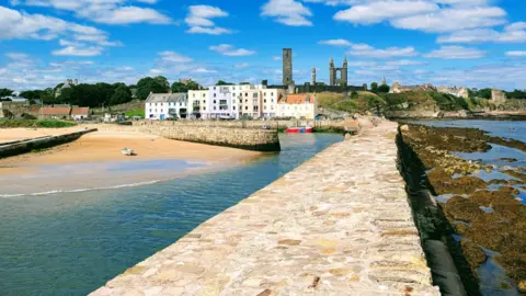 Tony Haverstock Harbour wall, with water either side, heading into the town of St Andrews, with historic buildings in the distance.