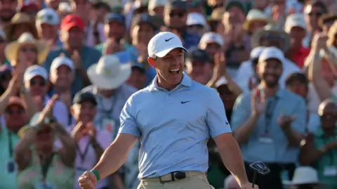 Reuters Rory McIlroy, a man with a blue polo shirt and white cap, celebrating a putt at The Masters in Augusta in April 2026.