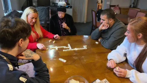 Five people sat round a table talking and playing dominoes, one of the groups which brings people together at The Crescent. 