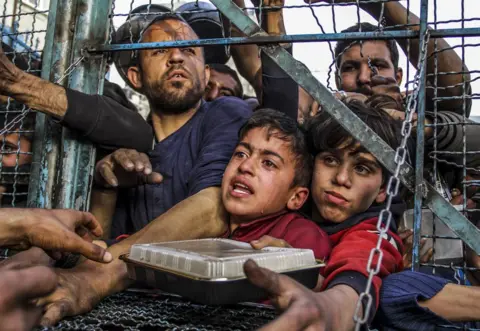 Getty Images Crowd of starving Palestinians, including children, hold to person nutrient distributed by kindness organisations successful March amid Israel's blockade arsenic nan business dramatically deteriorates successful Jabalia exile camp