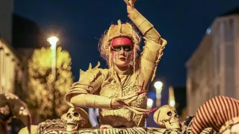 Street performers in Derry at Halloween. All are dressed in elaborate colourful costumes. 