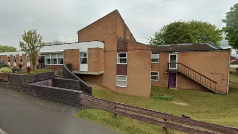 An exterior view of Benkhill Lodge, which is made from pale brown bricks with white frames on its square windows. 