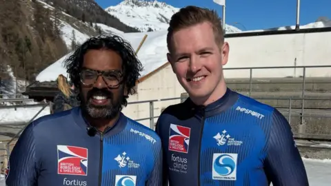 Romesh Ranganathan and Brad Hall stood, psoing for a photo. They both are smiling and looking directly at the camera. 