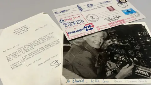 David Turner A letter addressed to "My dear David", thanking him for his "very nice letter". There is also a postcard with various stamps on it, and a photograph of the woman from the above picture in the cockpit of a plane. At the bottom of the picture it reads: "To David, with love from Cousin Sheila".