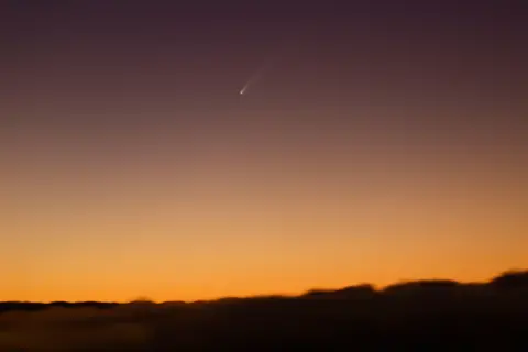 Reuters: A streak of yellow light far in the night sky, against a yellow haze. 