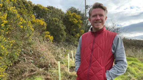 Ethical Schoolwear Liam Charlton-Killen wearing red fleece and grey sweatshirt beside hedges