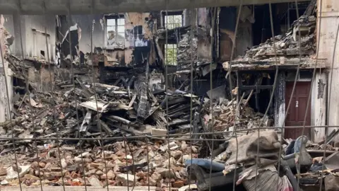 Mo Reeves Burned rubble and bricks sit alongside a red door which says '2A'