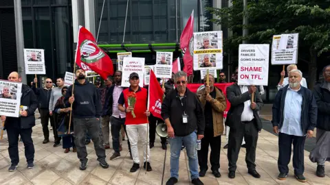 The protestors stand in a line holding up banners and pickets