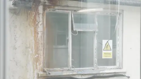A very old, broken hospital window, with a sign saying "Warning, fragile roof"