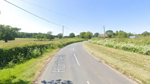 A stretch of country road with a single lane going in each direction, with fields on either side