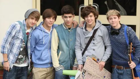 PA All five members of one Direction looking boyish in a picture from 2010, in which Harry Styles holds a sign written by a fan while a young Louis Tomlinson holds a guitar.