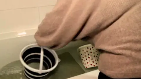 A person filling up a bucket out of a bath tub filled with water
