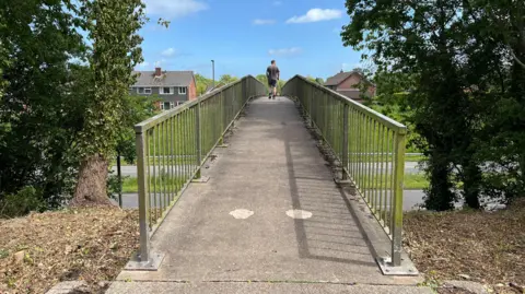 A man walks over the bridge with his back to the camera. 