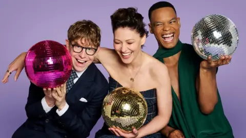 Josh Widdicombe, Emma Willis and Johannes Radebe holding glitter balls against a purple background