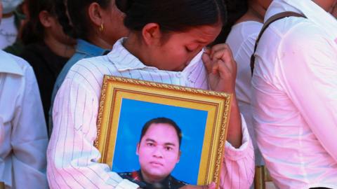 A woman weeps as she holds a photograph of one of the soldiers killed in an ammunition explosion at a C