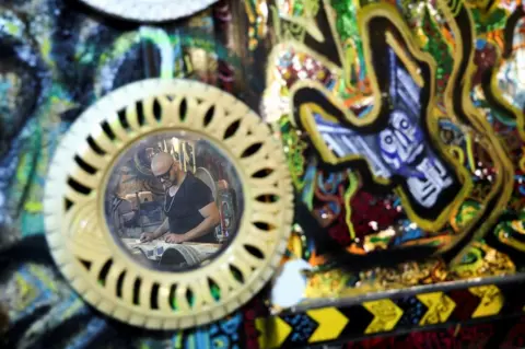 AMR ABDALLAH DALSH / REUTERS A man is reflected in a mirror made from recycled car tires. 