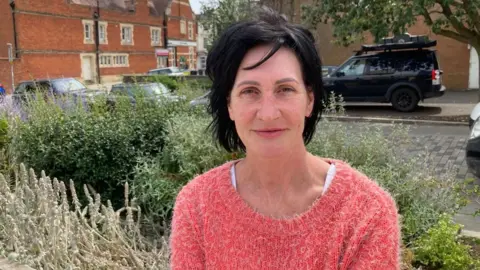 Martin Heath/BBC Erin Hills with dark hair and red top sitting in front of bushes