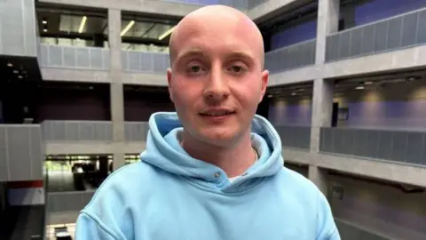 A young bald man wearing a light blue hoody.
