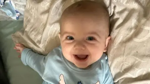 Baby Jensen smiles at the camera.