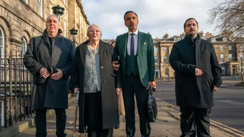 PA Media Emma's mother Margaret Caldwell, uncle Jim Coyle, nephew Stewart McGrory and lawyer Aamer Anwar address the media outside Bute House on a sunny day - all three family members are wearing dark coats while Ms Caldwell is holding a walking stick. Mr Anwar is wearing a green suit and is the person speaking.