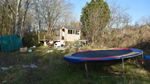 Met Police A wooden shed in a litter strewn and overgrown allotment, with a circular trampoline in the foreground.