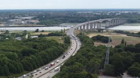 A drone image of the A14 looking toward the Orwell Bridge. The bridge can be seen in the distance. Queues of traffic can be seen on the carriageway.