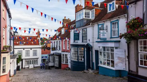 Row of shops in a cobbled stone street of grade II listed buildings.