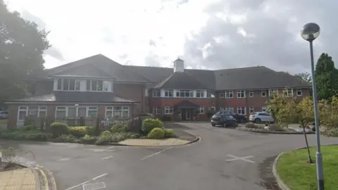 Coombe End Court Care Home in Marlborough. It is a brown brick building and there are bushes outside. 