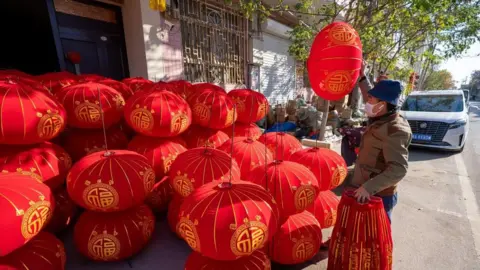 BBC/Benjamin Begley Chinese man standing in front of a pile of bright red Lunar New Year lanterns by the roadside