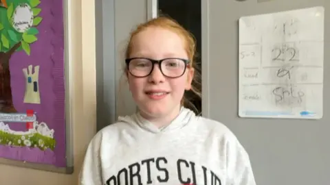 Sorsha, une jeune fille portant des lunettes à monture noire et une capuche grise